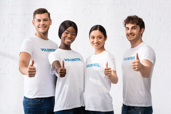 Multicultural volunteers looking at camera while showing thumbs up in charity center — Stock Photo