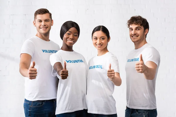 Volontari multiculturali che guardano la macchina fotografica mostrando i pollici in alto nel centro di beneficenza — Foto stock