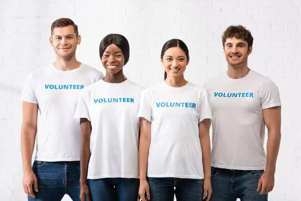 Jóvenes multiétnicos con letras de voluntarios en camisetas mirando a la cámara - foto de stock