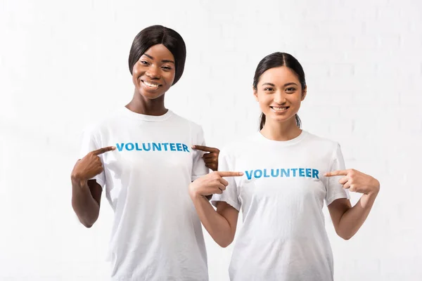 Africano americano e asiático voluntários apontando com os dedos para t-shirts — Fotografia de Stock