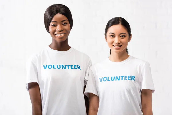Mulheres asiáticas e africanas americanas com letras voluntárias em camisetas olhando para a câmera — Fotografia de Stock