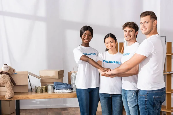 Young multiethnic volunteers holding hands and looking at camera in charity center — Stock Photo