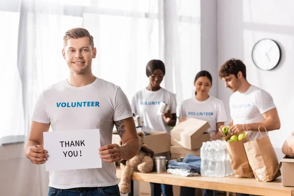 Enfoque selectivo de la tarjeta de retención de voluntarios con letras de agradecimiento en el centro de caridad - foto de stock