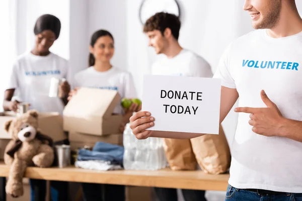 Selective focus of young volunteer pointing with finger at card with donate today lettering in charity center — Stock Photo