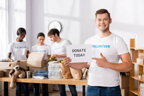 Focus selettivo del volontario che punta al biglietto con donare oggi lettering nel centro di beneficenza — Foto stock