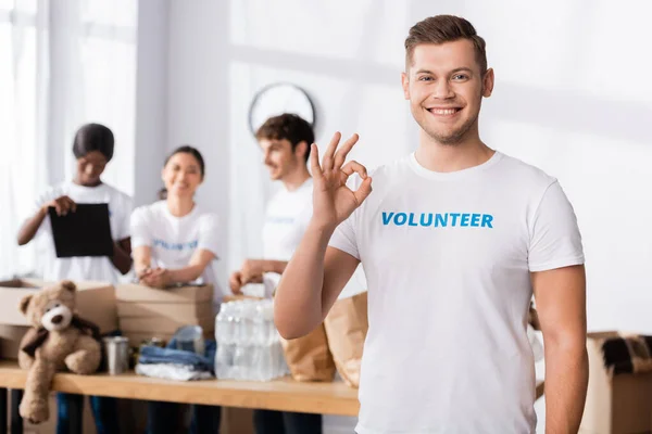 Enfoque selectivo del voluntario mostrando un gesto aceptable en la cámara en el centro de caridad - foto de stock