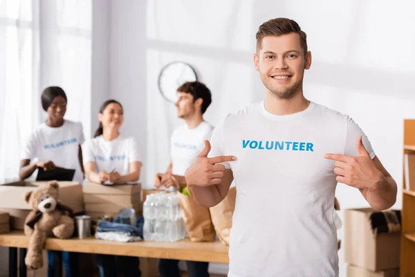 Selective focus of volunteer looking at camera and pointing with fingers at t-shirt with lettering — Stock Photo