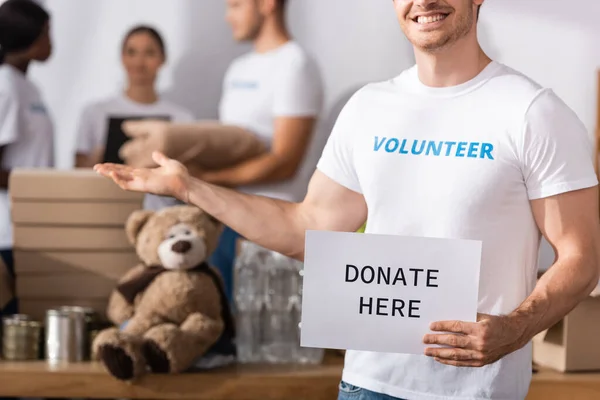 Enfoque selectivo de la tarjeta de tenencia de voluntarios con donar hoy letras y señalar con la mano en el centro de caridad - foto de stock