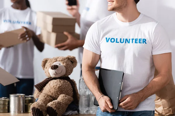 Vista ritagliata di volontariato tenendo appunti vicino lattine e peluche nel centro di beneficenza — Foto stock