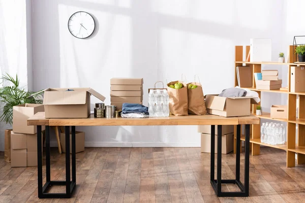 Tin cans, clothes and carton boxes on table in charity center — Stock Photo