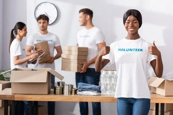 Enfoque selectivo del voluntariado afroamericano mostrando como personas cercanas multiculturales y donaciones en el centro de caridad - foto de stock