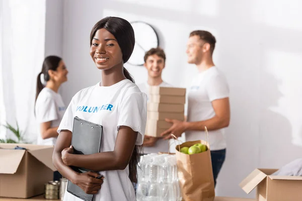 Selective focus of african american volunteer holding clipboard near donations in charity center — Stock Photo