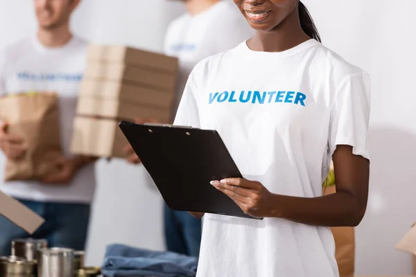 Vista recortada de mujer afroamericana en camiseta con escritura de letras voluntarias en portapapeles - foto de stock