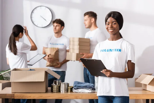 Селективный фокус африканской американки в футболке с надписью добровольца, держащей планшет в благотворительном центре — стоковое фото