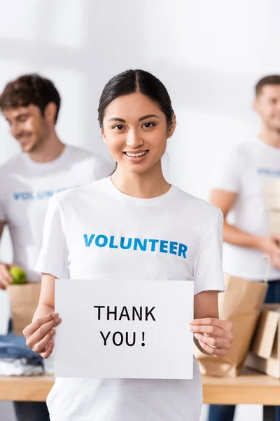 Selective focus of asian volunteer holding card with thank you lettering in charity center — Stock Photo