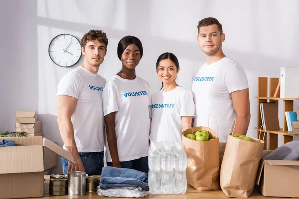 Enfoque selectivo de voluntarios multiétnicos mirando a la cámara cerca de donaciones en la mesa - foto de stock