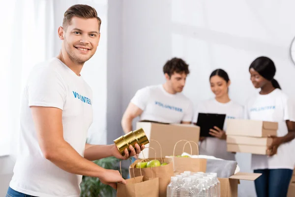 Selective focus of volunteer holding tin cans near packages in charity center — Stock Photo