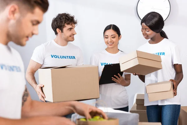 Selective focus of multiethnic volunteers holding clipboard and boxes in charity center — Stock Photo