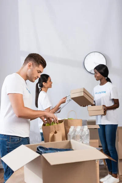 Selective focus of volunteer putting apples in paper bags in charity center — Stock Photo