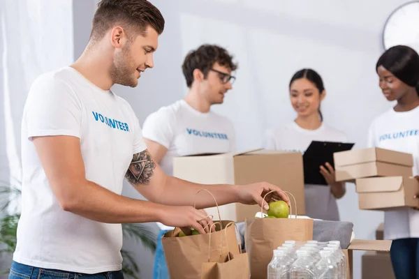 Concentration sélective d'un bénévole tenant des pommes près de sacs en papier dans un centre de bienfaisance — Photo de stock