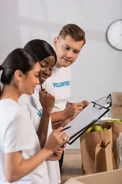 Selective focus of multiethnic volunteers looking at clipboards in charity center — Stock Photo