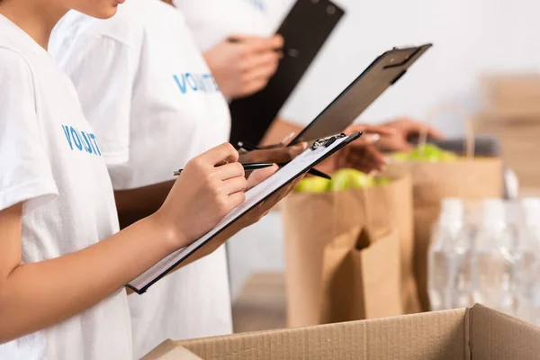 Cropped view of multiethnic volunteers holding clipboards in charity center — Stock Photo