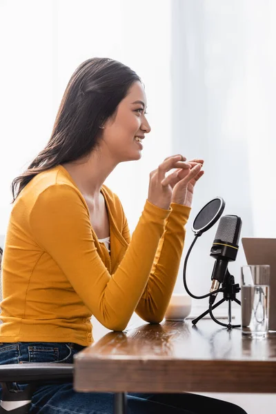 Selective focus of asian broadcaster showing small amount gesture while sitting near microphone in studio — Stock Photo