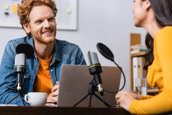 Enfoque selectivo de anfitrión de radio pelirroja emocionada entrevistando a mujer joven en el estudio - foto de stock