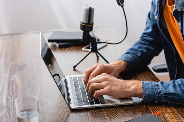 Cropped view of broadcaster typing on laptop near microphone at workplace — Stock Photo