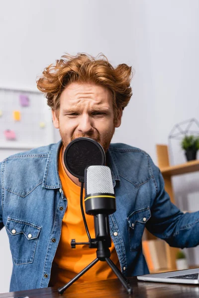 Annunciatore teso rossa in camicia denim parlando in microfono sul posto di lavoro — Foto stock
