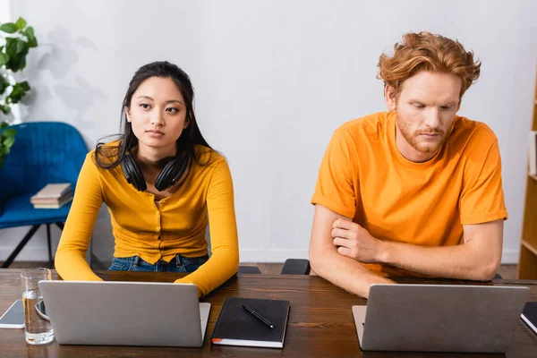 Pareja interracial de freelancers reflexivos usando computadoras portátiles en casa - foto de stock