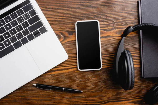 Vista superior do smartphone com tela em branco, laptop, fones de ouvido sem fio, notebook e caneta na mesa de escritório — Fotografia de Stock