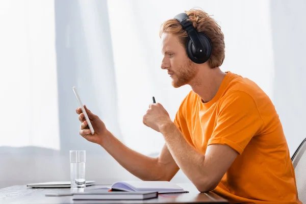 Visão lateral do estudante pensativo em fones de ouvido sem fio usando tablet digital em casa — Fotografia de Stock