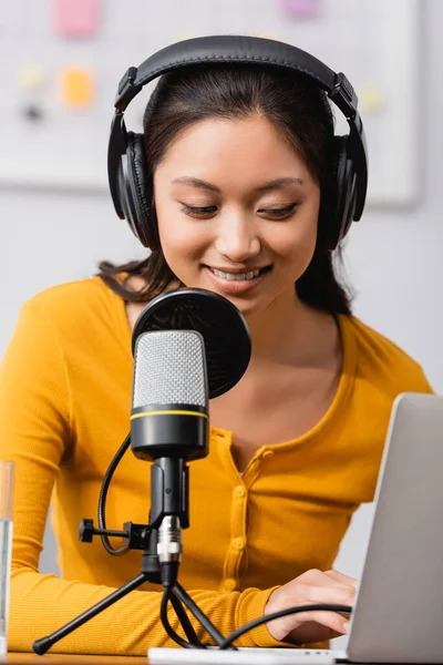 Foyer sélectif du diffuseur asiatique dans les écouteurs sans fil tapant sur ordinateur portable près du microphone — Photo de stock