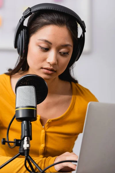 Вибірковий фокус концентрованого азіатського мовника в бездротових навушниках за допомогою ноутбука поблизу мікрофона — стокове фото