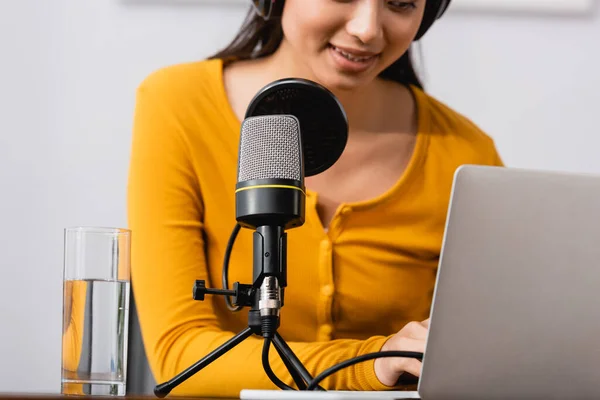 Vista parziale di asiatica annunciatore digitando sul computer portatile vicino al microfono in studio radio — Foto stock