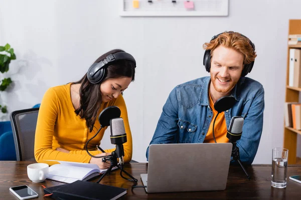 Junge interrassische Sender in drahtlosen Kopfhörern, die im Radiostudio in der Nähe von Mikrofonen arbeiten — Stockfoto