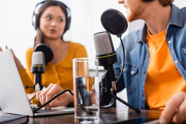 Selective focus of asian broadcaster in wireless headphones talking to colleague in radio studio — Stock Photo