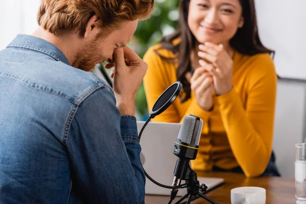 Selective focus of excited asian radio host looking at confused man touching face during interview — Stock Photo