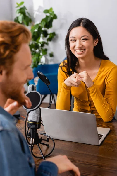 Selective focus of excited asian interviewer looking at guest in radio studio — Stock Photo