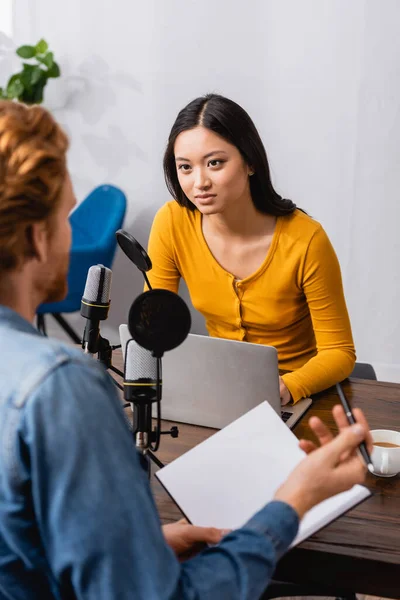 Back view of man holding notebook and pen during interview with young asian broadcaster — Stock Photo