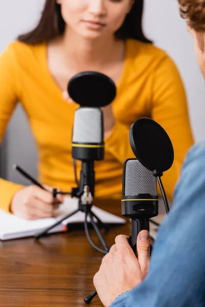 Cropped view of broadcaster writing in notebook during interview with guest in studio — Stock Photo