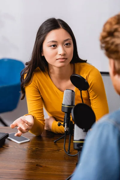 Selective focus of young asian broadcaster gesturing during interview with man in radio studio — Stock Photo