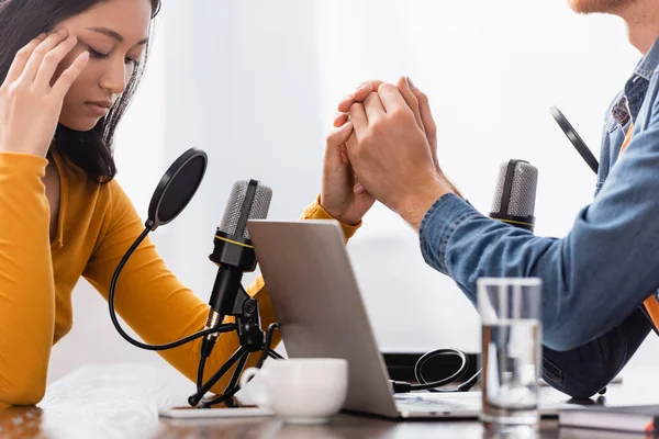 Broadcaster holding hand of upset asian woman touching head during interview — Stock Photo