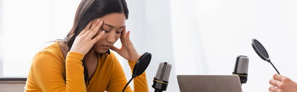 Animateur radio près bouleversé asiatique femme avec les yeux fermés toucher la tête pendant entrevue, concept horizontal — Photo de stock