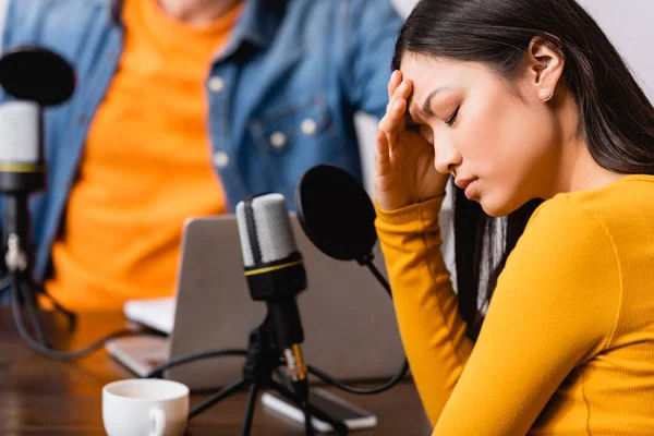 Foco seletivo de host de rádio perto chateado asiático mulher tocando cabeça durante entrevista — Fotografia de Stock