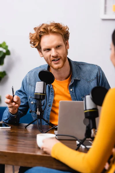 Selektiver Fokus von Frau und rothaarigem Interviewer, der Stift in der Hand hält und am Mikrofon spricht — Stockfoto