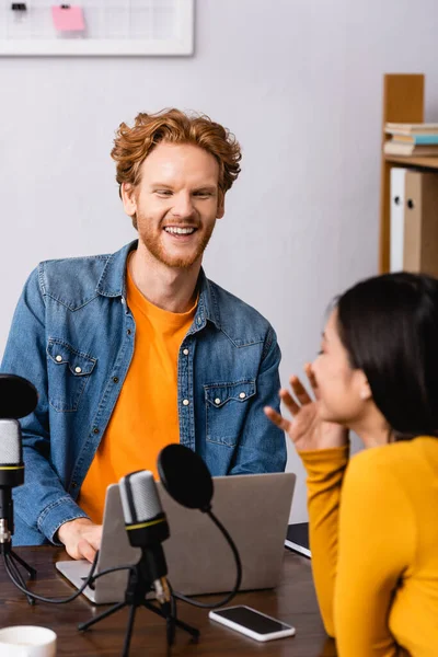 Anfitrião de rádio animado rindo enquanto entrevistava jovem morena em estúdio — Fotografia de Stock