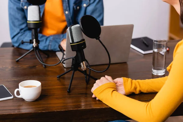 Cropped view of interviewer and guest near microphones and laptop in radio studio — Stock Photo