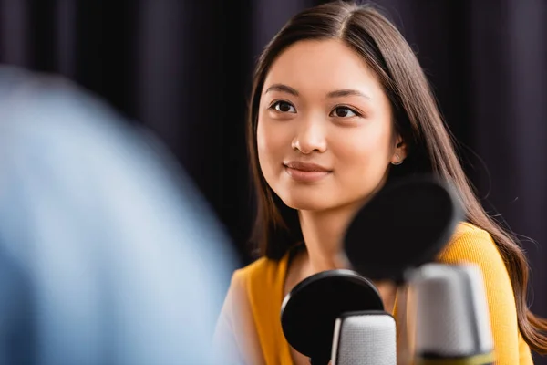 Selective focus of young, brunette asian broadcaster near microphone in radio studio — Stock Photo